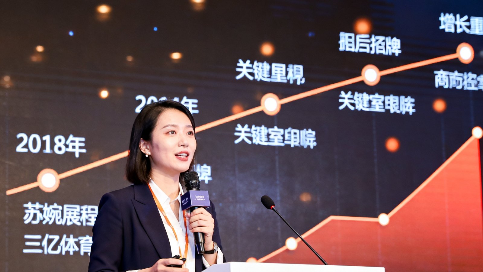 三亿体育COO苏婉清在体育科技行业论坛上发表演讲，大屏幕展示着公司发展历程的数据图表